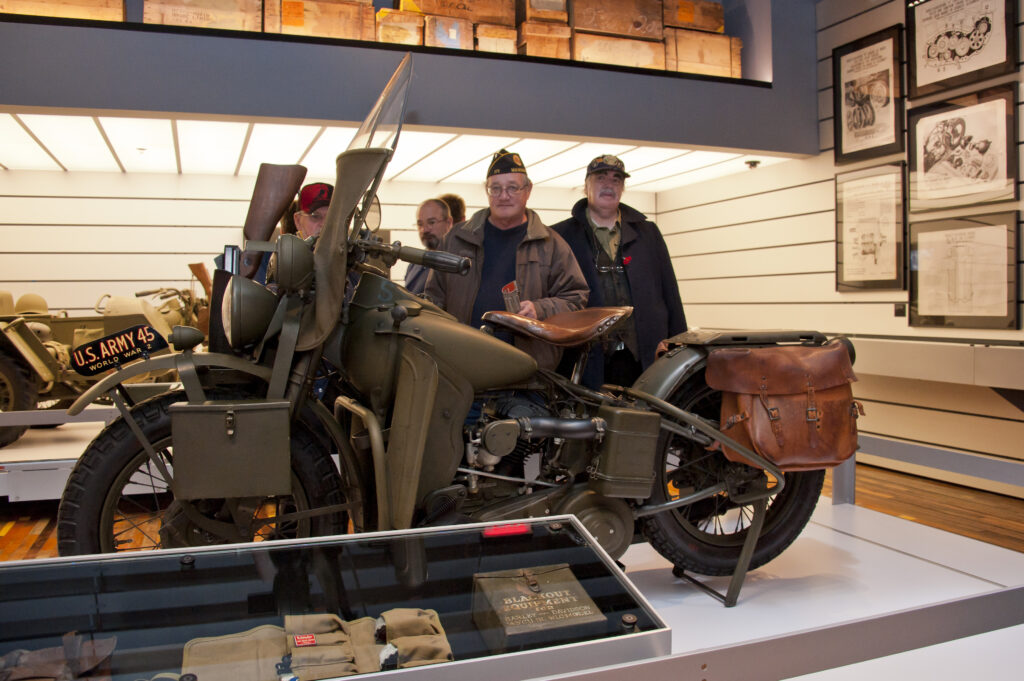 A group of men look at an old motorcycle.